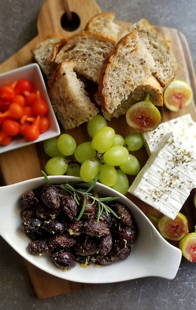 Baked Kalamata Olives with feta cheese, grapes, figs and bread on a cutting board