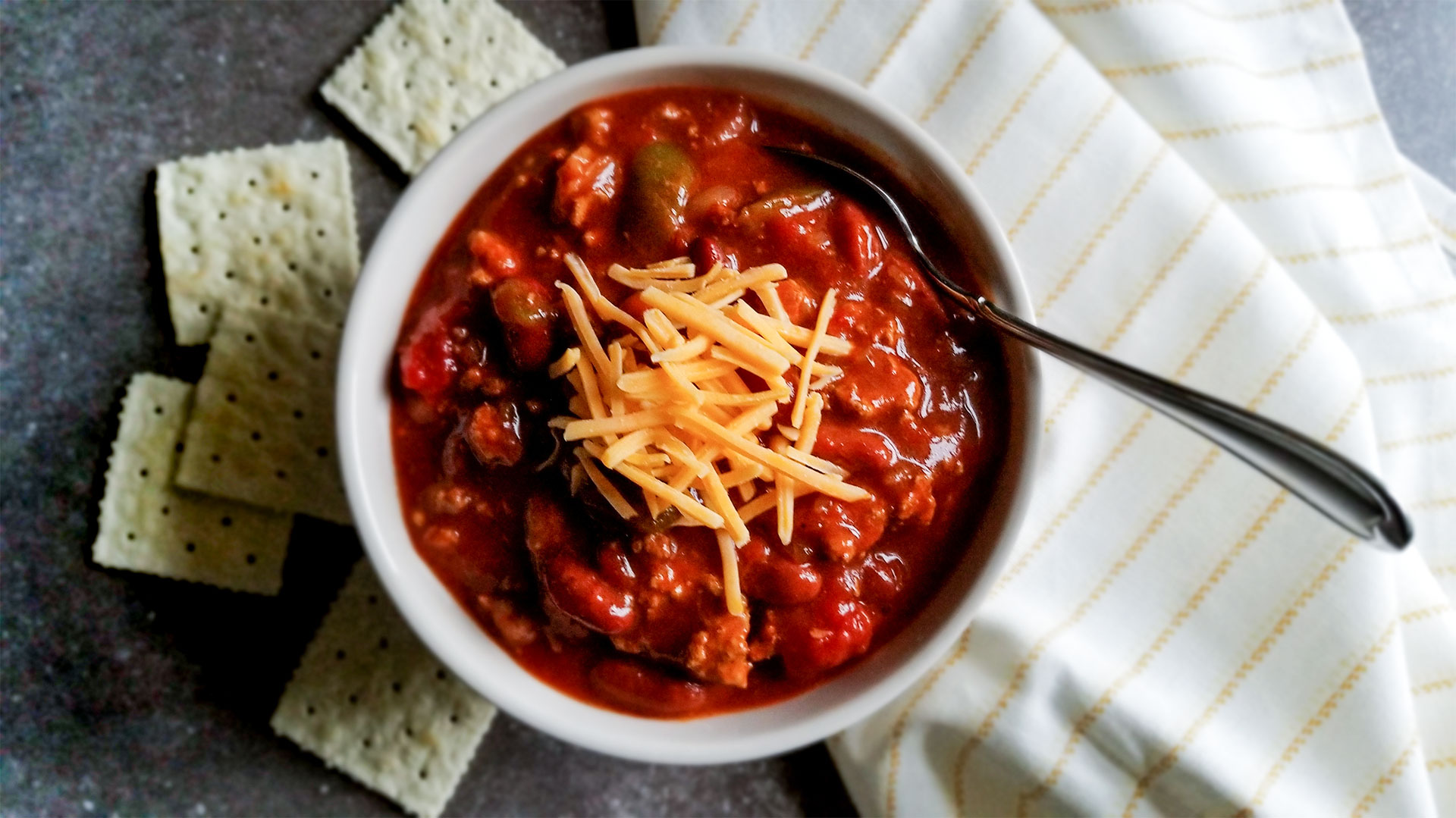 Turkey Chili in a bowl topped with cheese served with crackers