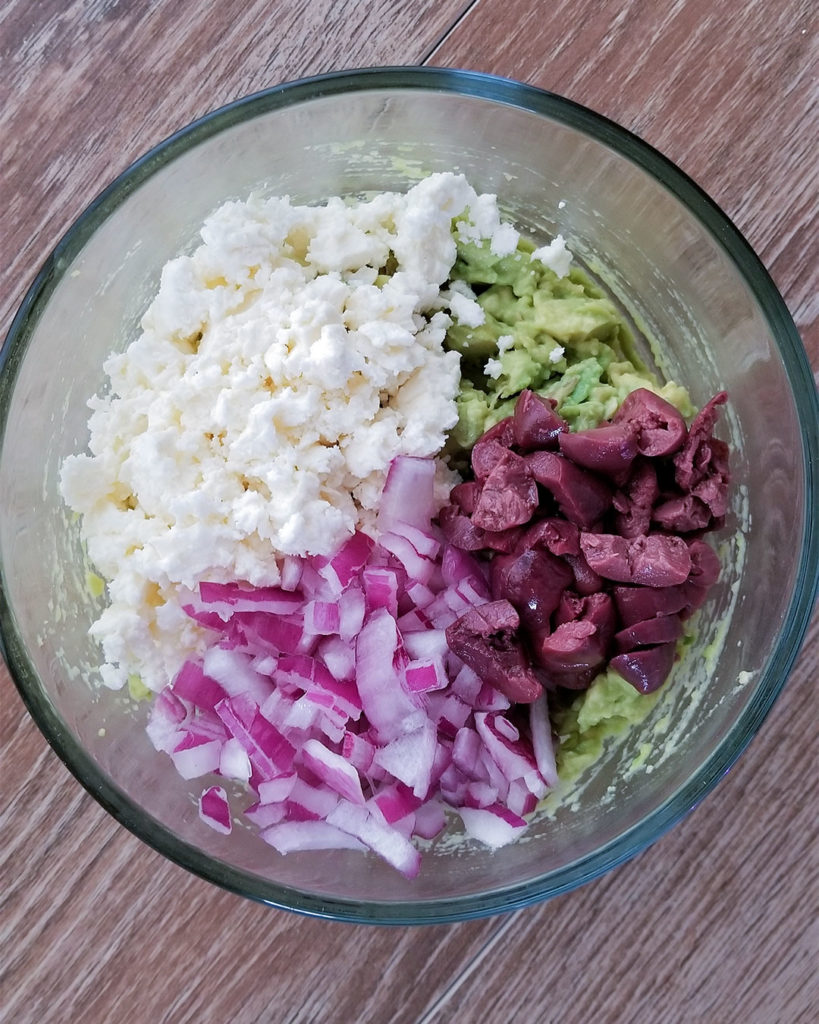 mashed avocados, feta cheese, Kalamata olives and red onion in a bowl