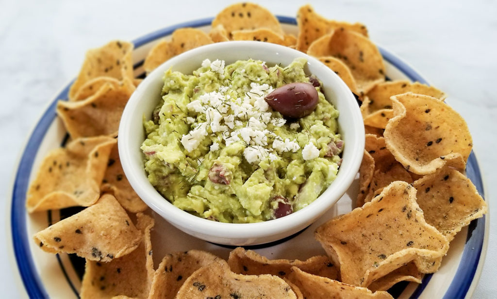 Greek Style Guacamole topped with feta cheese in a bowl with chips