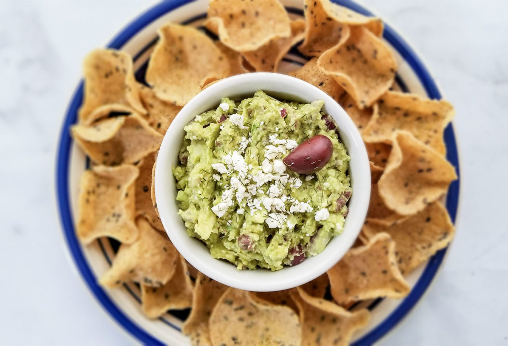 Greek Style Guacamole topped with feta cheese in a bowl with chips