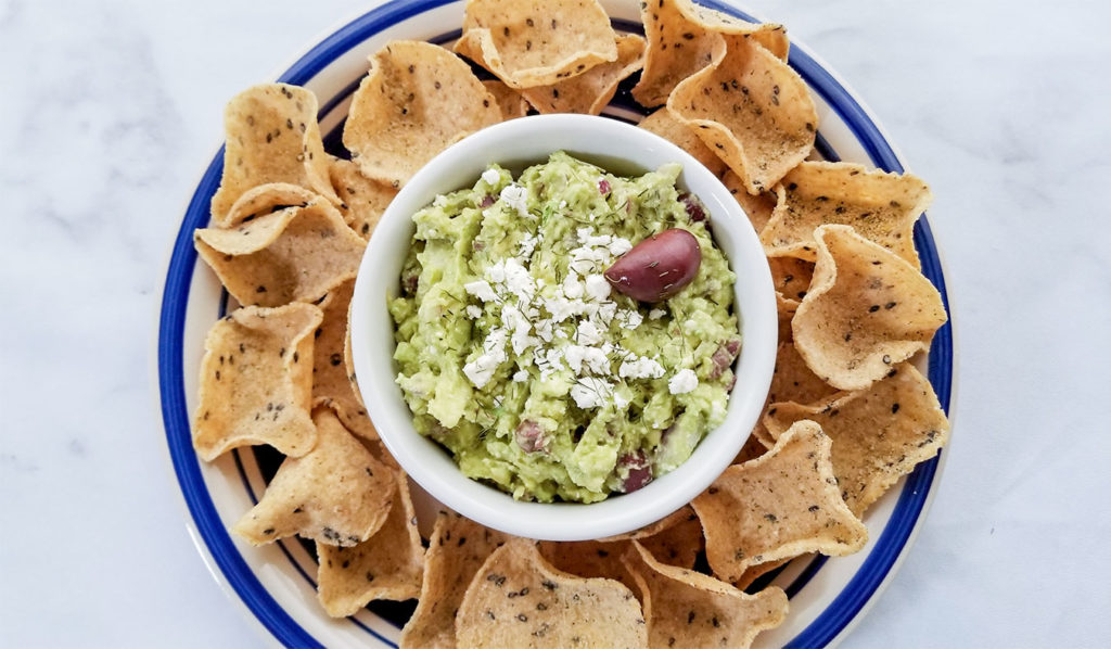 Greek Style Guacamole topped with feta cheese in a bowl with chips