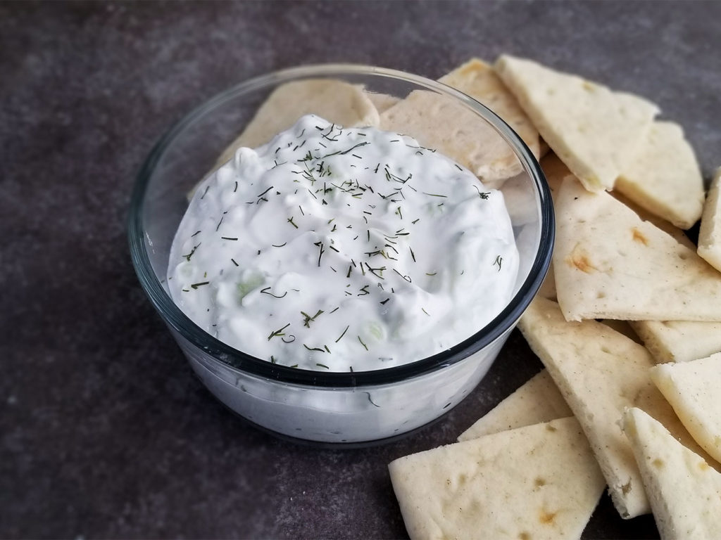 Tzatziki Sauce in a bowl topped with dill alongside pita bread