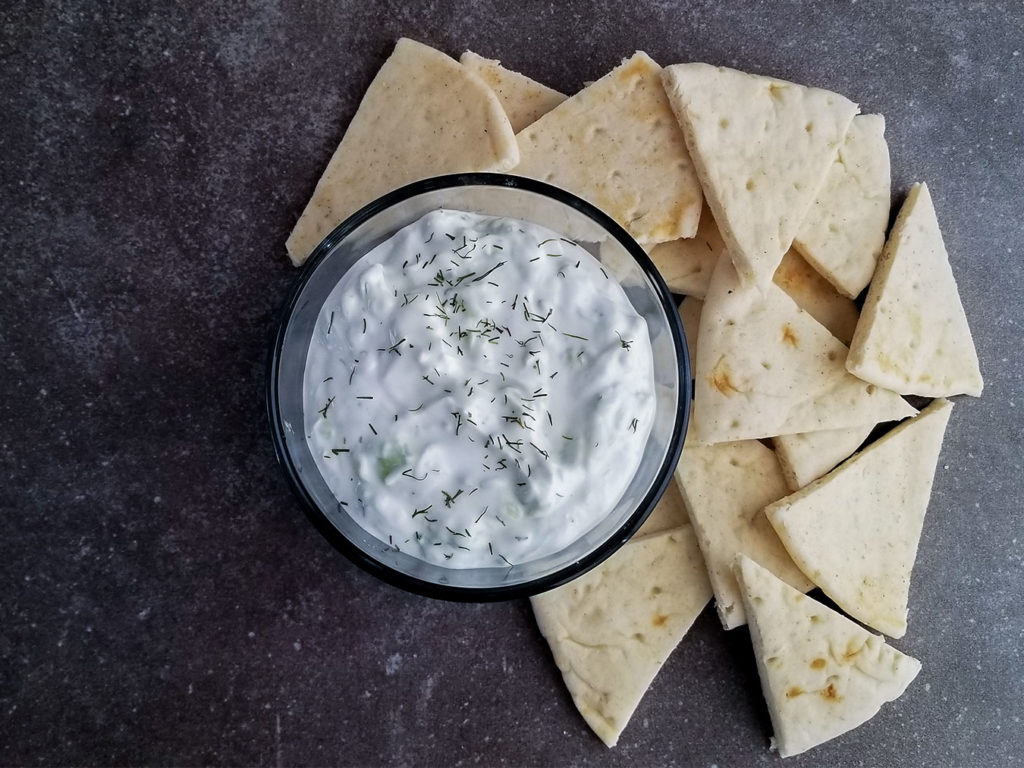 Tzatziki Sauce in a bowl topped with dill alongside pita bread