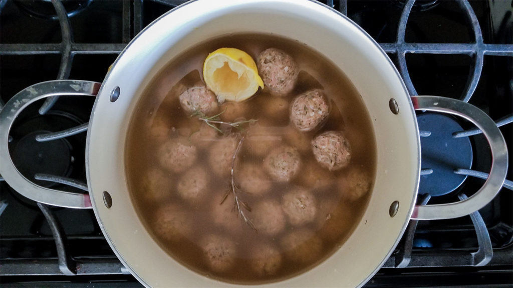 Youvarlakia meatballs in a stockpot with chicken broth, rosemary and lemon