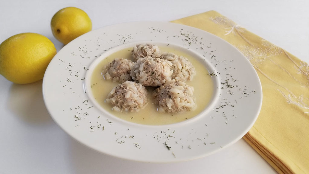 Youvarlakia (Greek Meatball Soup) in a bowl with lemons