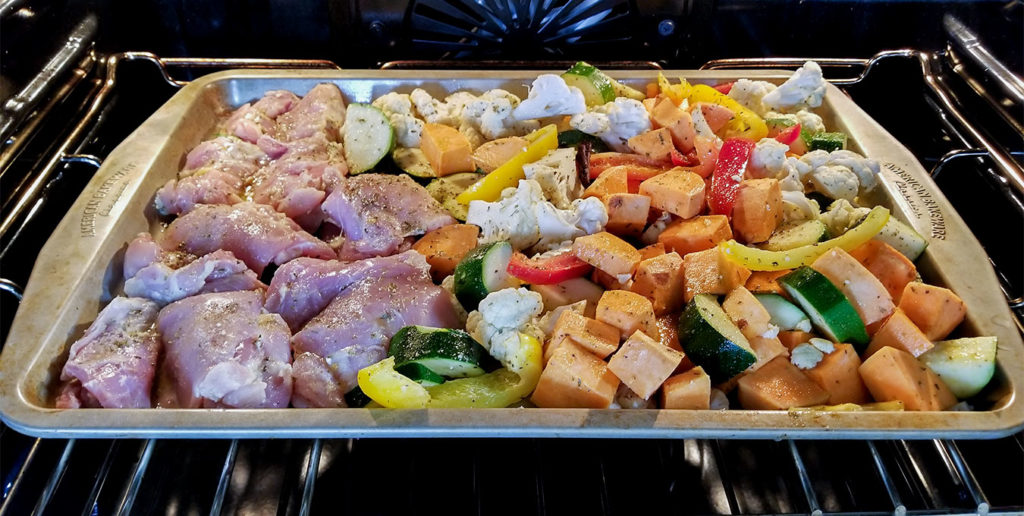 vegetables and chicken on a sheet pan roasting in the oven