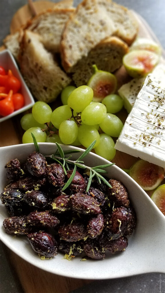 Baked Kalamata Olives with feta cheese, grapes, figs and bread on a cutting board