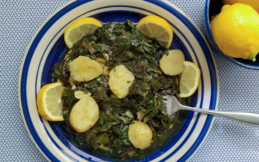 Greek greens with potatoes in a bowl with lemon wedges
