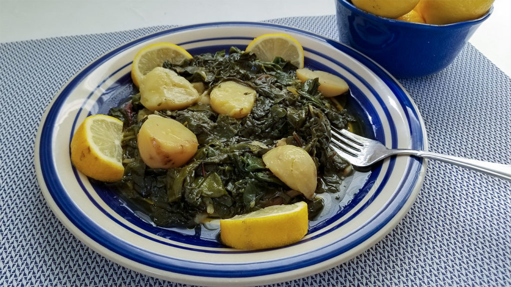 Greek greens with potatoes in a bowl with lemon wedges