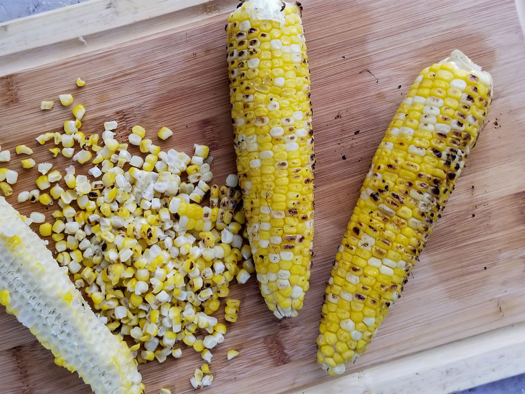grilled corn on the cob being cut in a cutting board