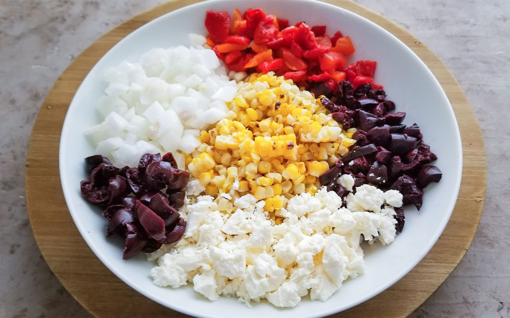 Grilled Greek Corn Salad ingredients in a bowl before mixing