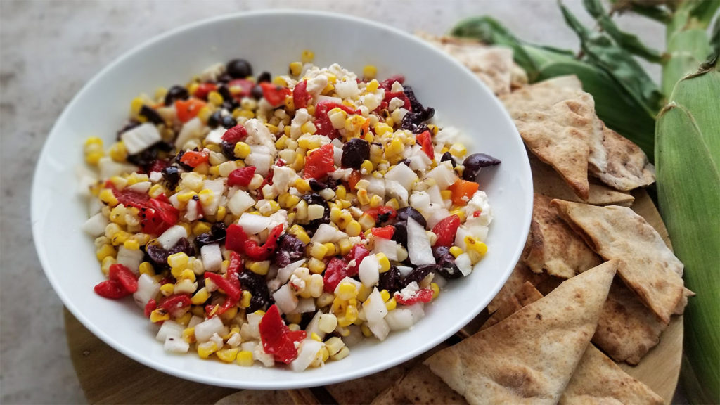 Grilled Greek Corn Salad in a bowl with homemade pita chips