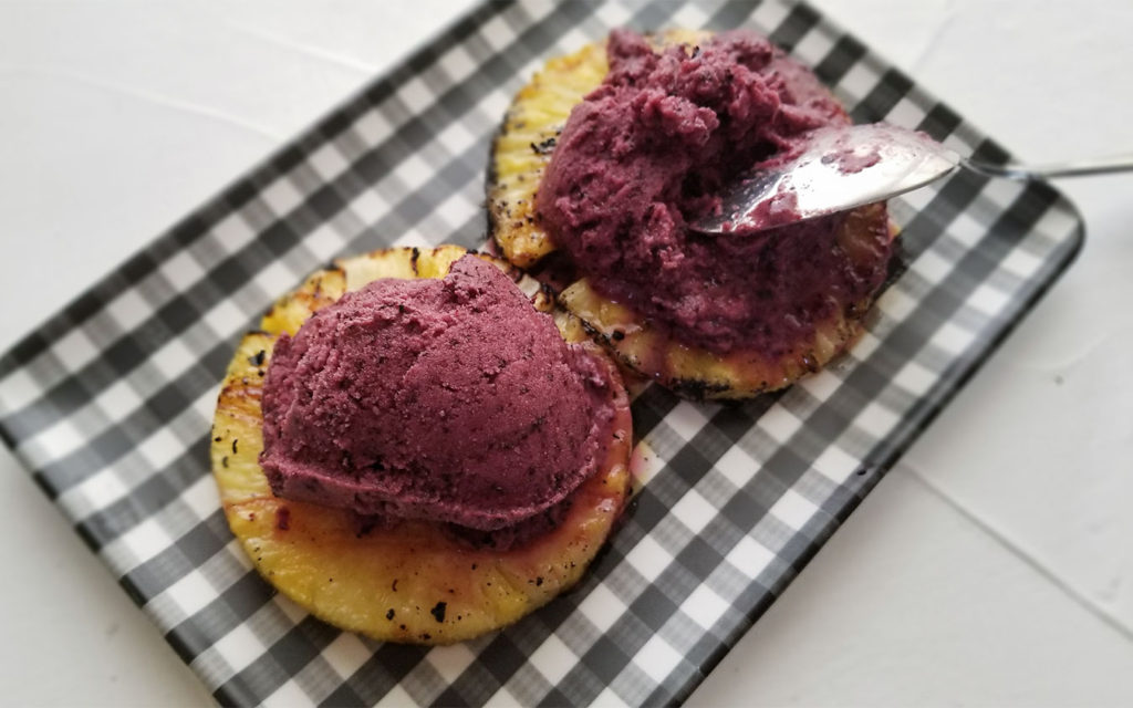 Grilled Pineapple topped with Frozen Blueberry Yogurt on a plate with a spoon