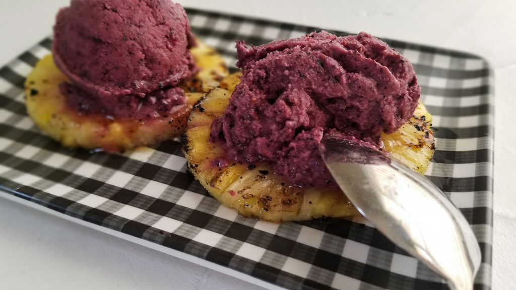 Grilled Pineapple topped with Frozen Blueberry Yogurt on a plate with a spoon