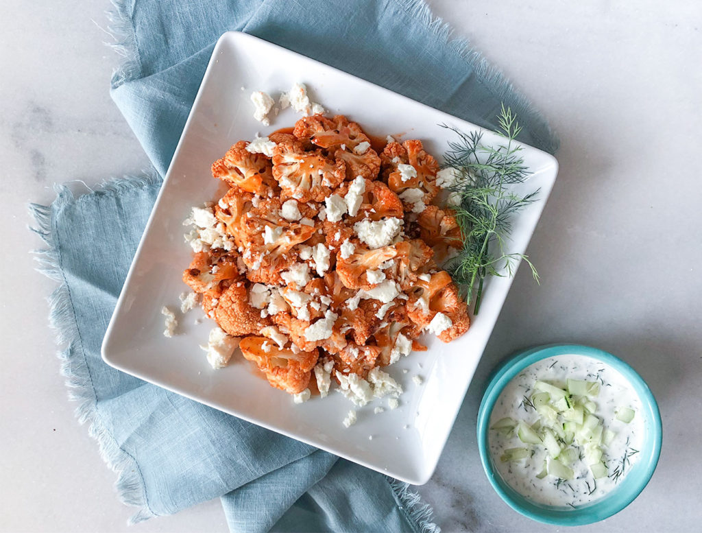 Buffalo Cauliflower on a plate topped with feta cheese with a side of tzatziki sauce