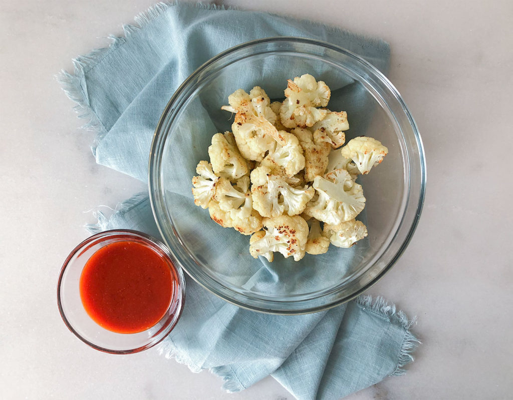 baked cauliflower in a bowl with buffalo sauce in a smaller bowl