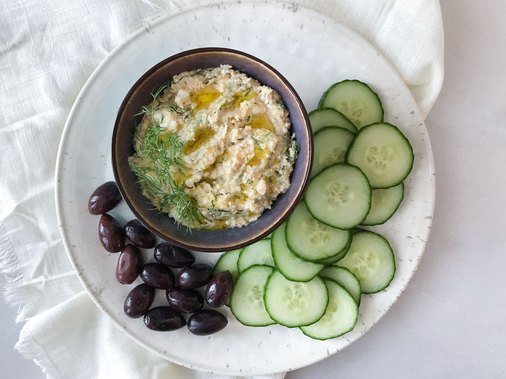 Greek Hummus in a bowl with cucumber slices and Kalamata olives