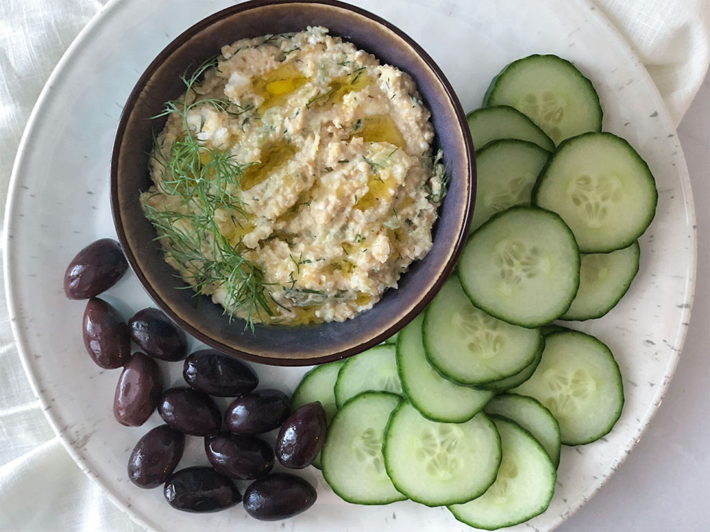 Greek Hummus in a bowl with cucumber slices and Kalamata olives