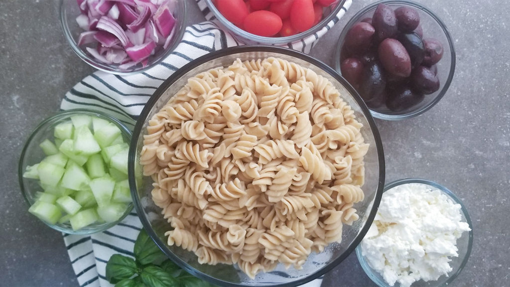 Greek pasta salad ingredients in bowls