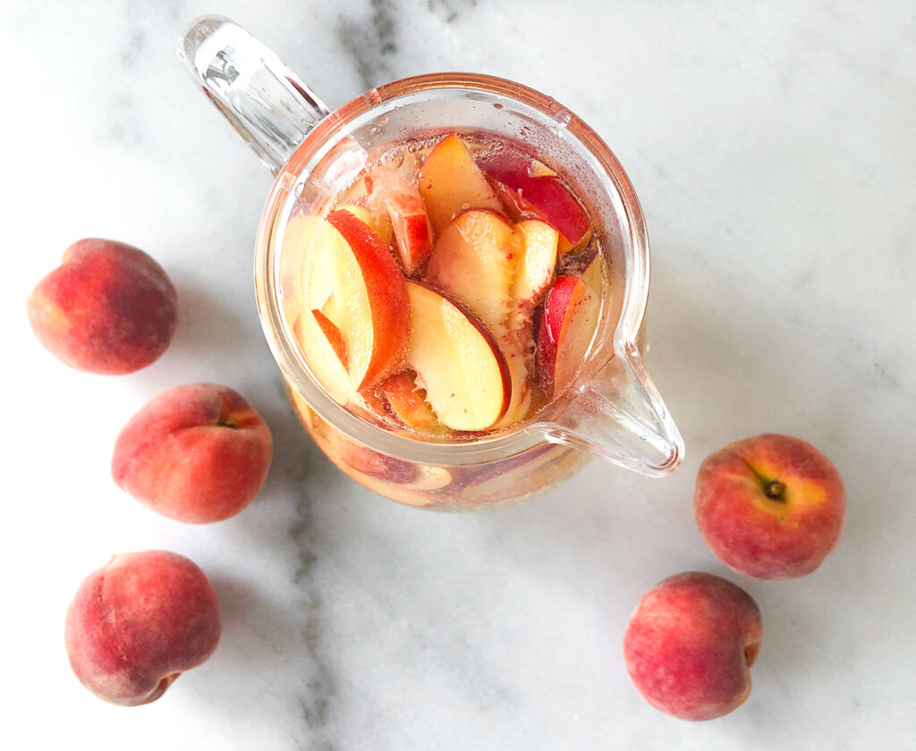 Peach Sangria in a pitcher with whole peaches on a table