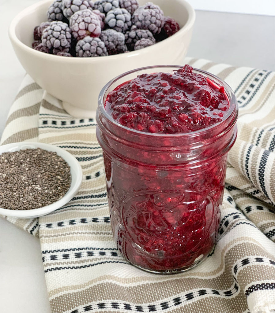 Blackberry Chia Jam in a mason jar with frozen blackberries in a bowl
