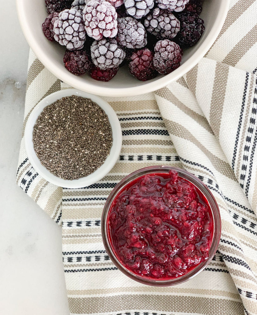 Blackberry Chia Jam in a mason jar with frozen blackberries in a bowl