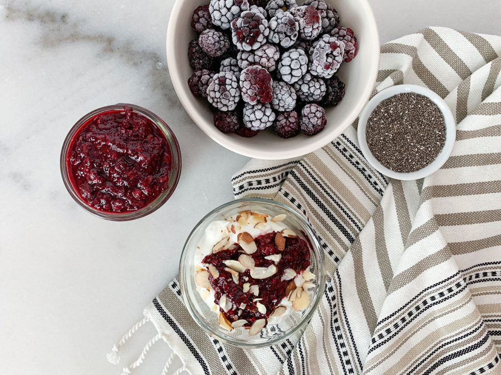 Blackberry Chia Jam on top of greek yogurt and in a mason jar with frozen blackberries in a bowl