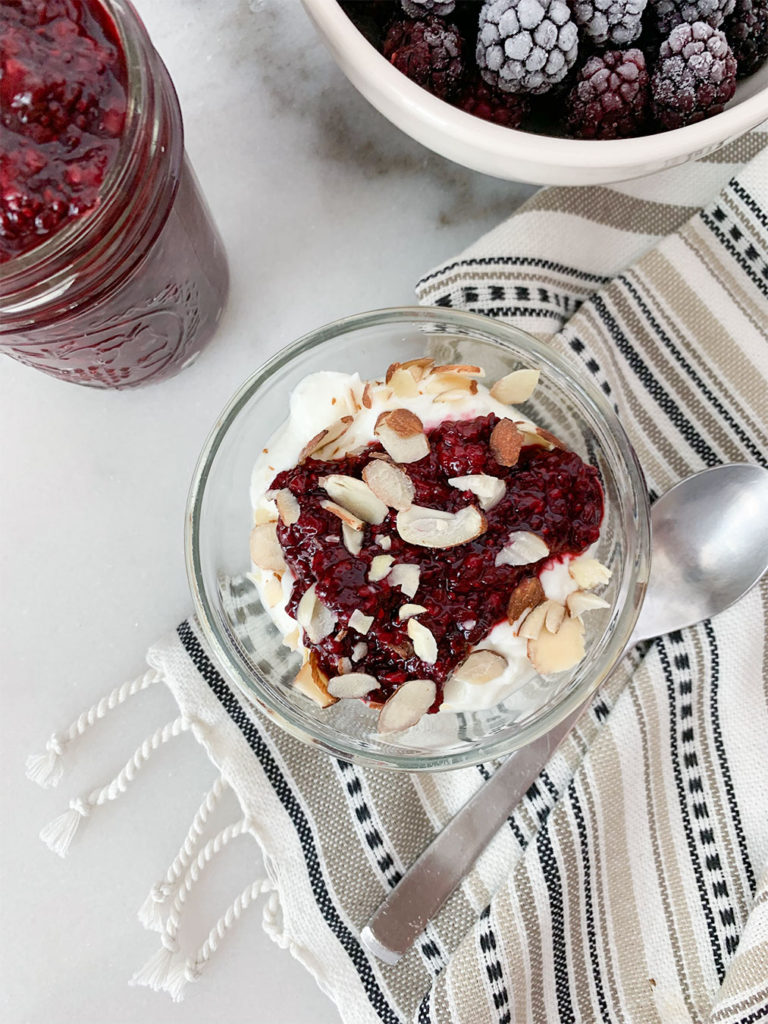Blackberry Chia Jam on top of greek yogurt and in a mason jar with frozen blackberries in a bowl