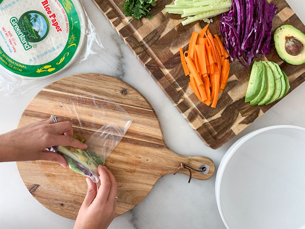 rolling rice paper wrappers filled with Vegetable Summer Rolls ingredients on a cutting board