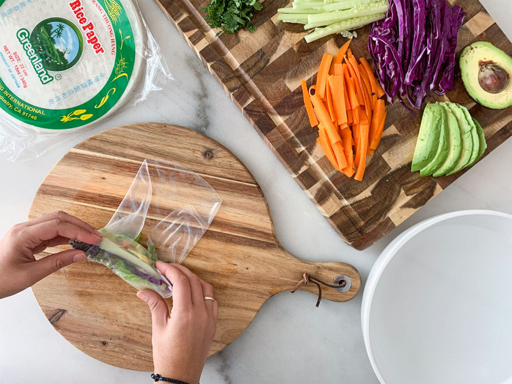 rolling rice paper wrappers filled with Vegetable Summer Rolls ingredients on a cutting board