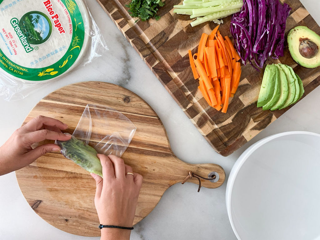 rolling rice paper wrappers filled with Vegetable Summer Rolls ingredients on a cutting board