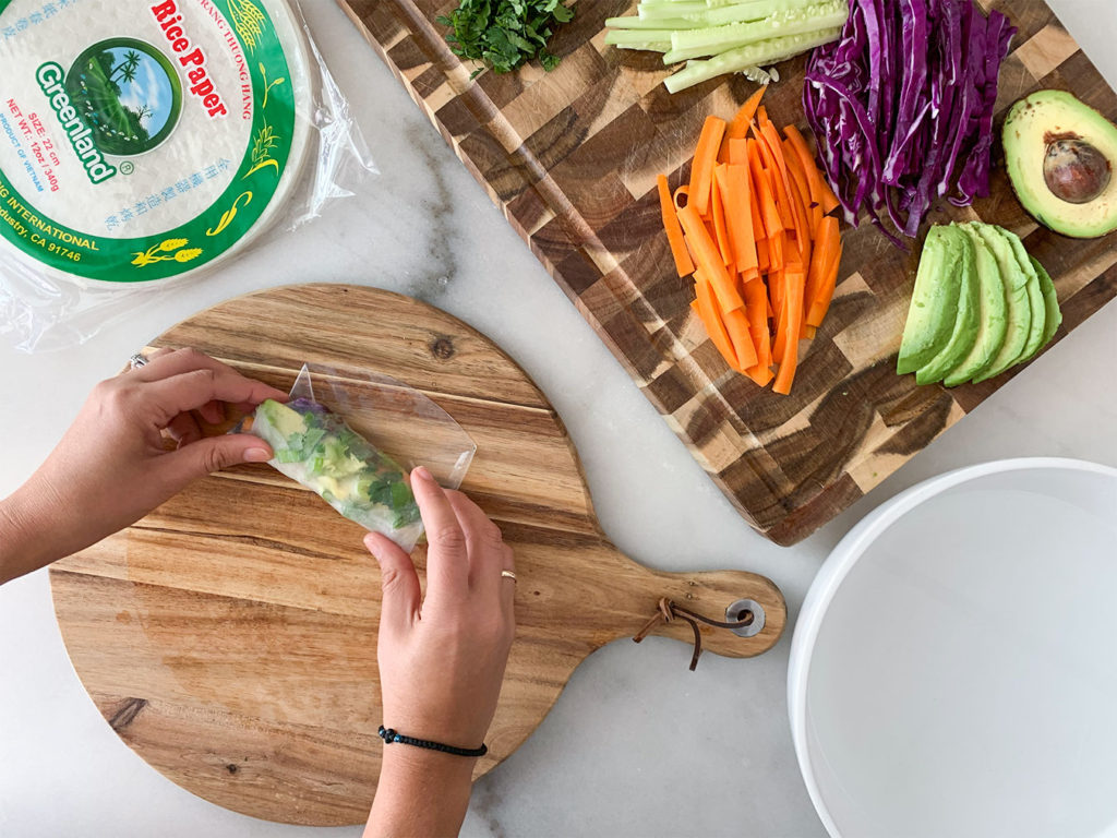 rolling rice paper wrappers filled with Vegetable Summer Rolls ingredients on a cutting board