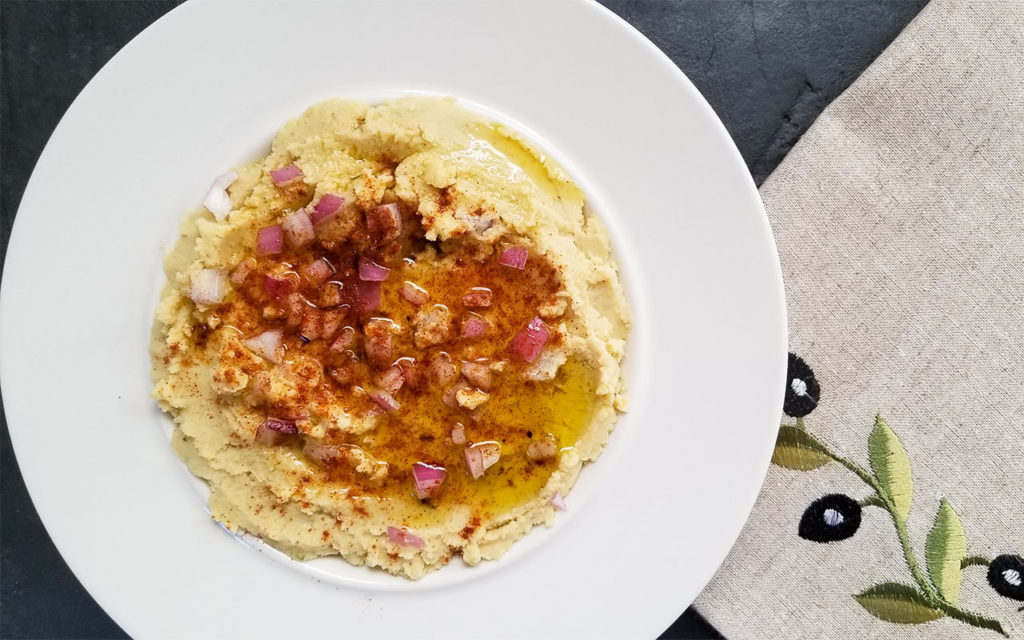 Fava dip in a bowl topped with red onion and olive oil