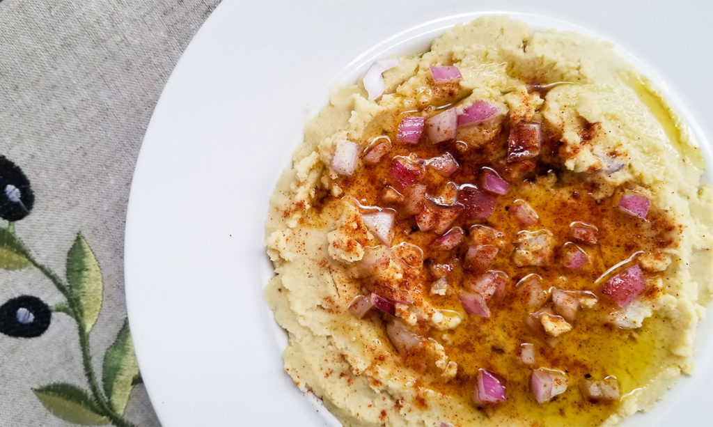 Fava dip in a bowl topped with red onion and olive oil