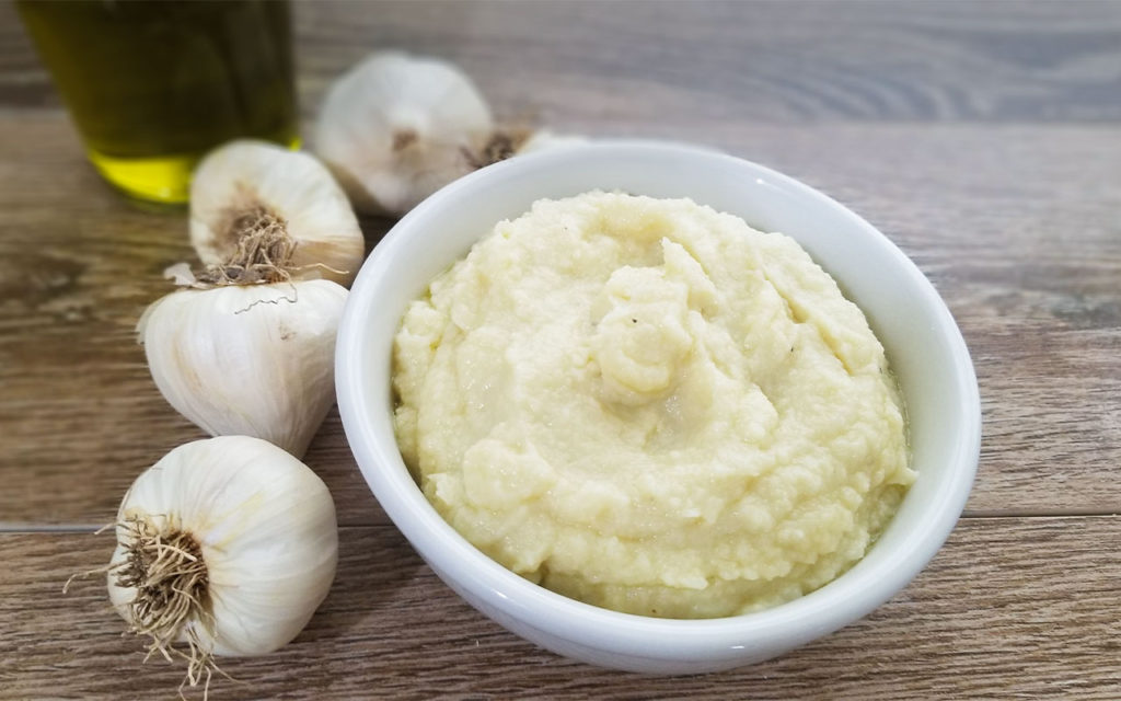 Skordalia in a bowl with garlic and olive oil