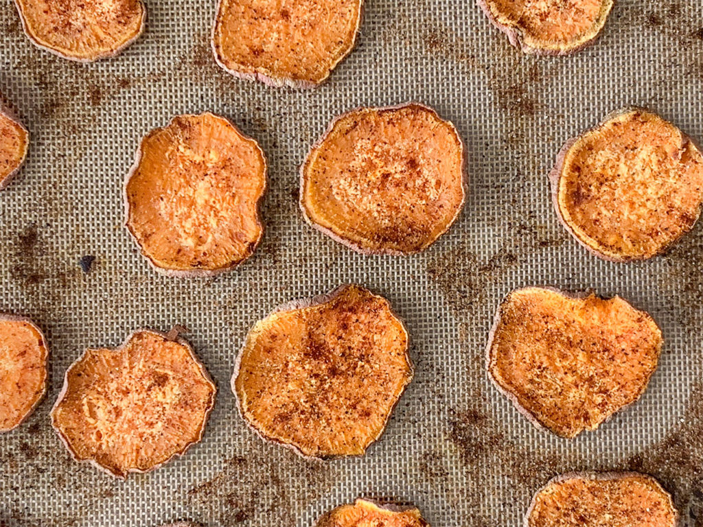 thinly sliced sweet potatoes on a silicone lined baking sheet with seasoning