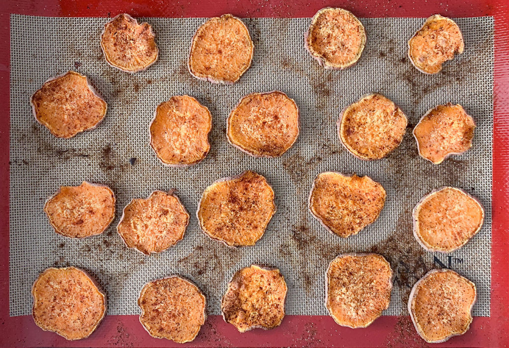 thinly sliced sweet potatoes on a silicone lined baking sheet with seasoning