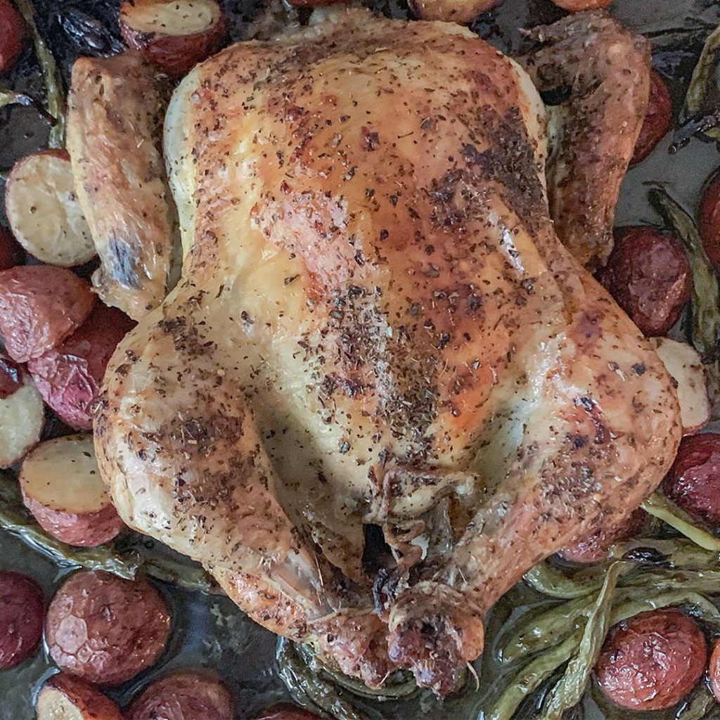whole roasted chicken on a baking sheet with vegetables