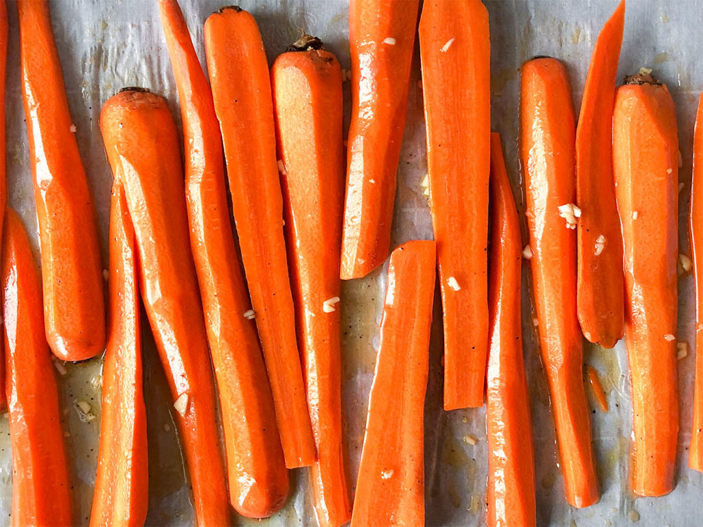 carrots cut in half on a baking sheet topped with a vinaigrette 