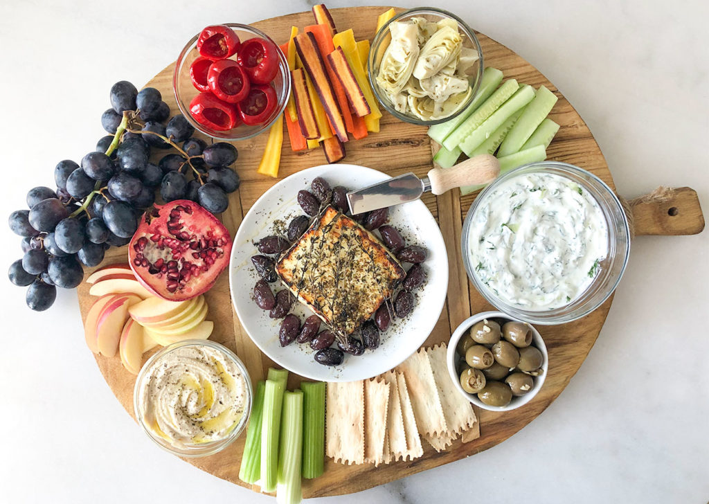 Baked feta, hummus, tzatziki and a variety of fruits and vegetables on a platter