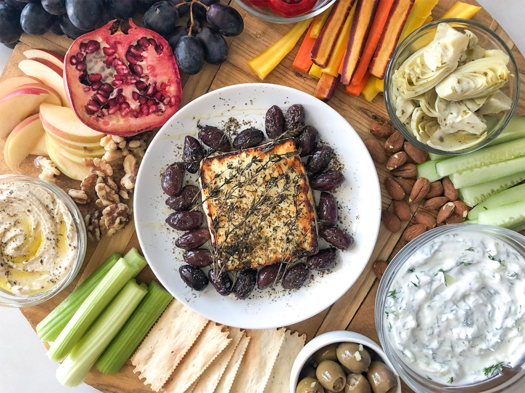 Baked feta, hummus, tzatziki and a variety of fruits and vegetables on a platter