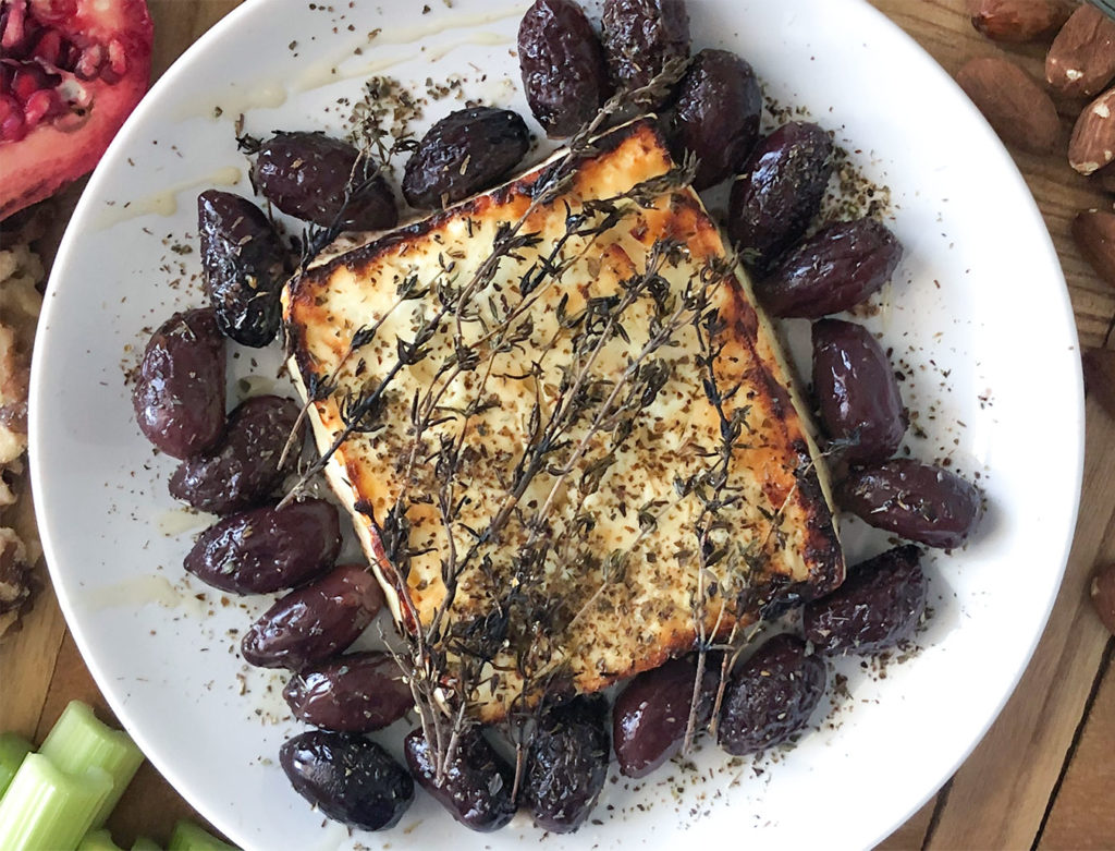 Baked feta with olive, oregano and thyme on a plate