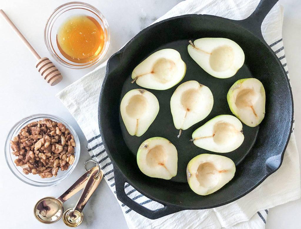 halved pears in a cast iron skillet with honey and walnuts