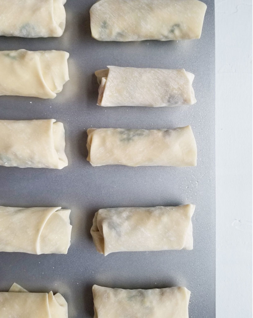 assembled egg rolls on a baking sheet