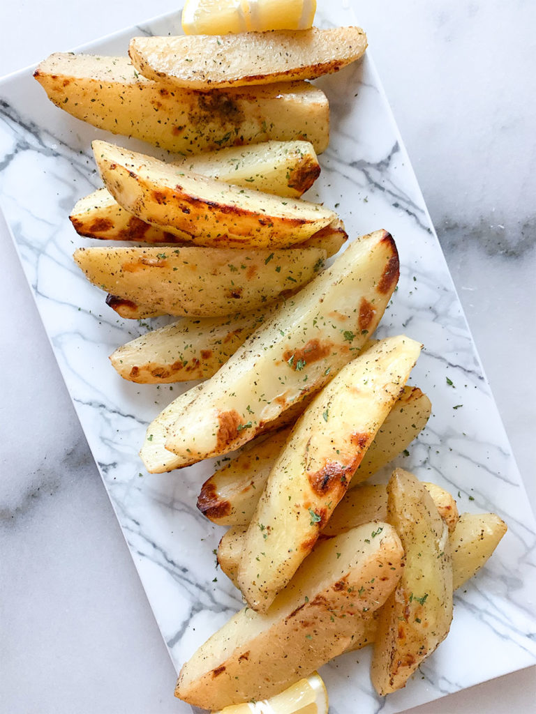 Greek lemon potatoes arranged on a plate with lemon wedges