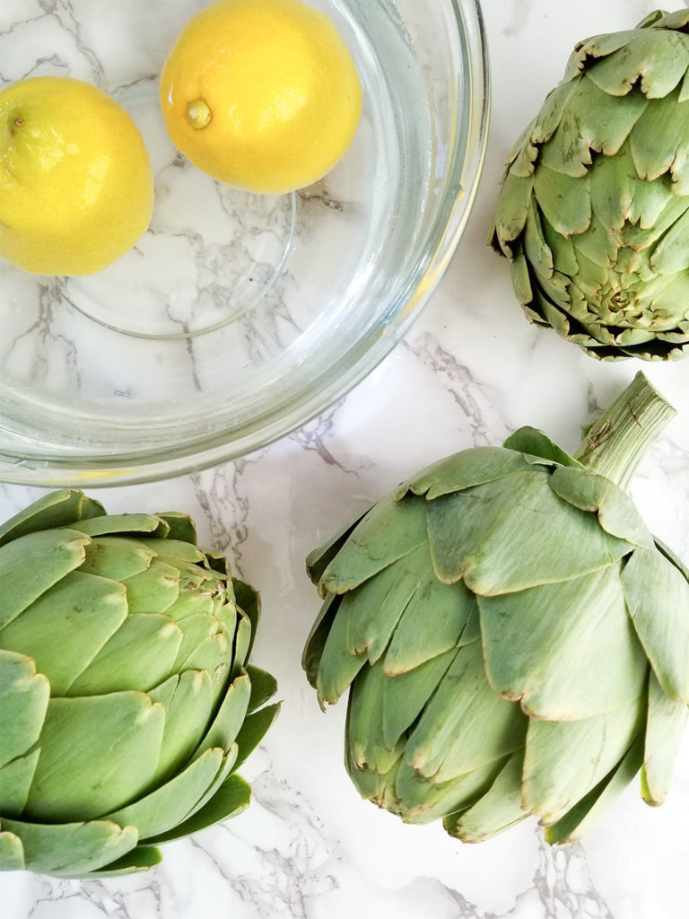 whole artichokes and a bowl of water with lemons
