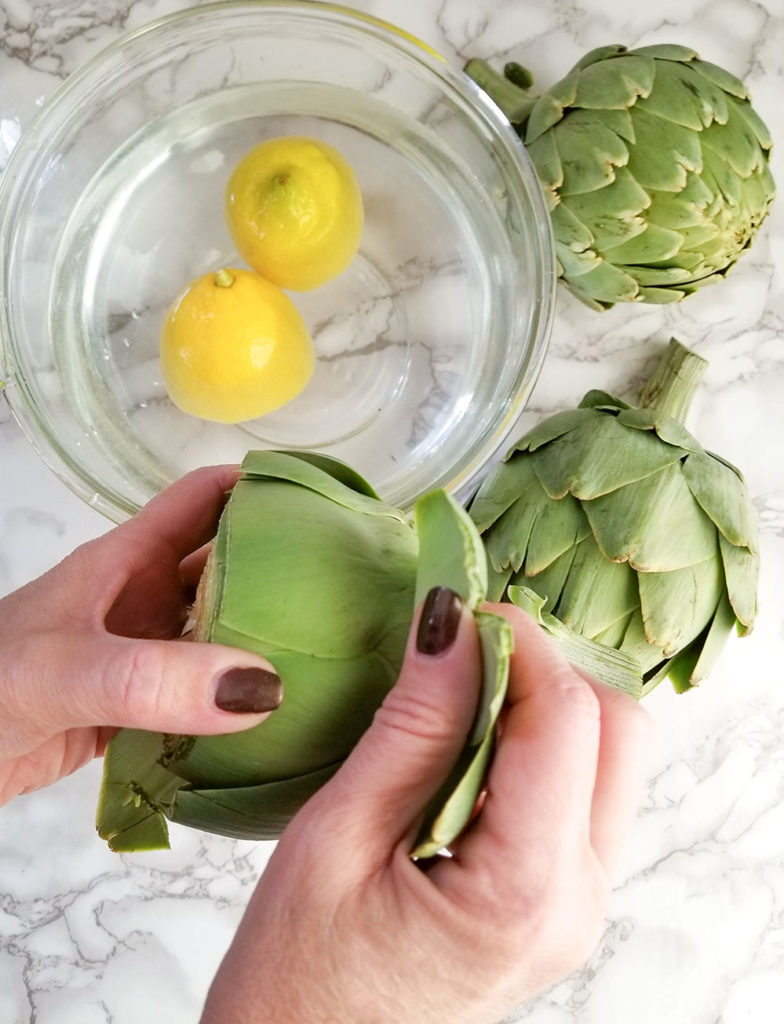 peeling whole artichokes and a bowl of water with lemons