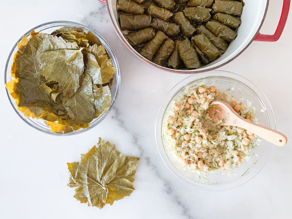 Stuffed grape leaves in a pot, grape leaves in a bowl, rice and chickpea filling in a bowl and rolling grape leaves