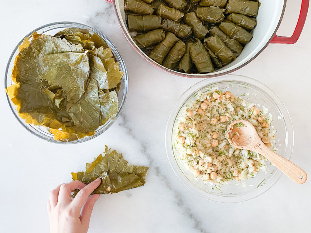 Stuffed grape leaves in a pot, grape leaves in a bowl, rice and chickpea filling in a bowl and rolling grape leaves